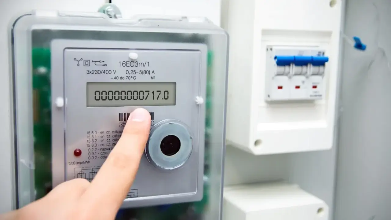 Palec wskazuje licznik prądu, pokazując jak odczytać licznik prądu. Widoczny jest odczyt 00000000717.0 kWh.