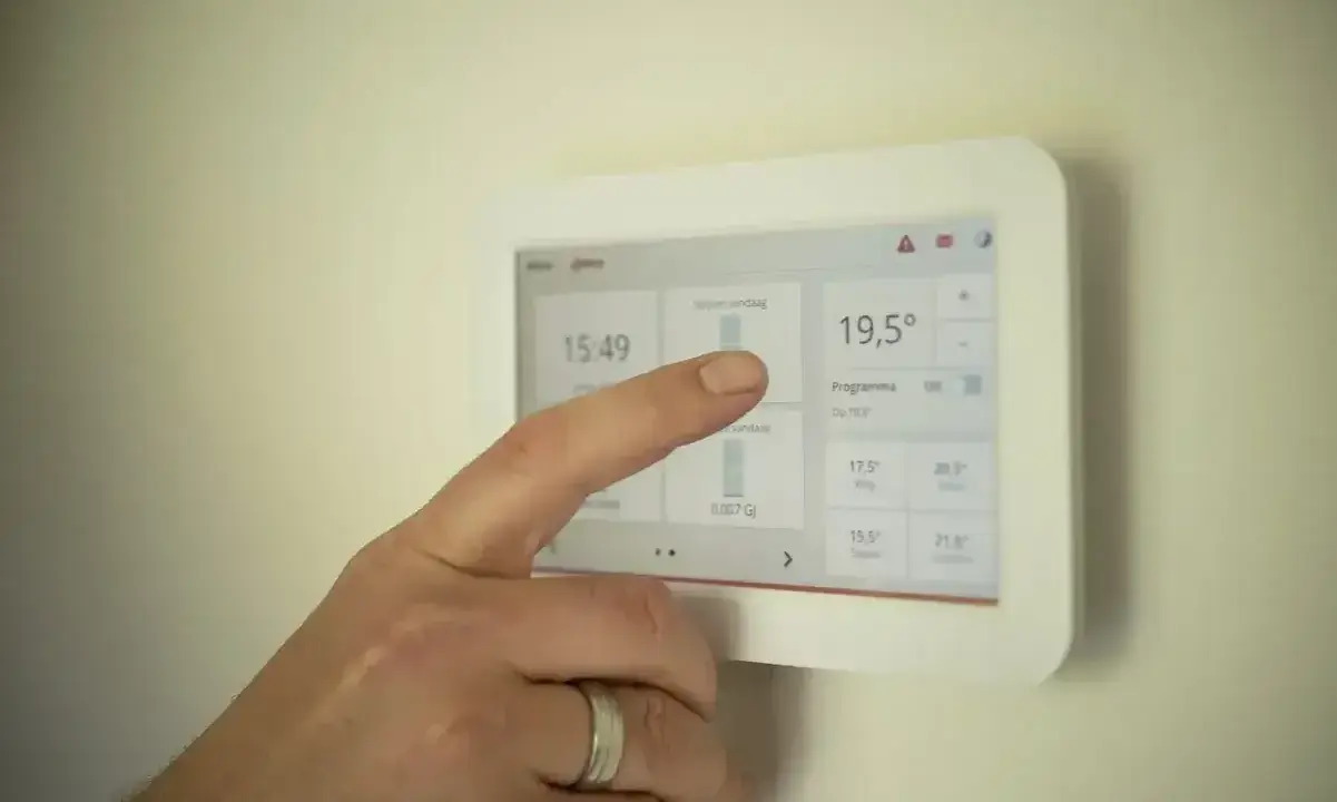 Dłoń dotyka ekranu termostatu, pokazując temperaturę 19,5°C. Ustawienia ogrzewania pomogą określić, jak często powinien włączyć się piec gazowy.