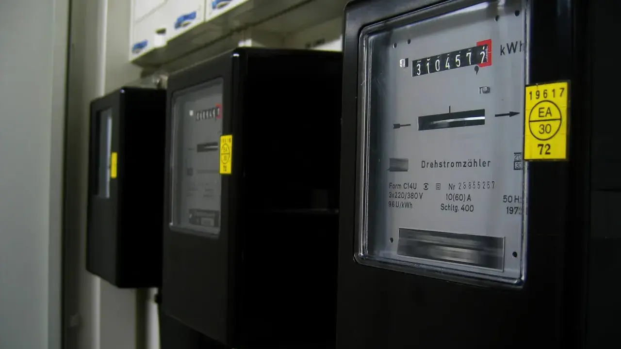 Trzy czarne liczniki energii elektrycznej z cyfrowymi wyświetlaczami i żółtymi naklejkami.
