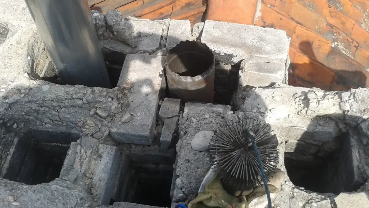 Widok na komin z widocznym metalowym czopuchem i szczotką do czyszczenia. Prawidłowe podłączenie czopucha do komina jest kluczowe dla bezpieczeństwa.