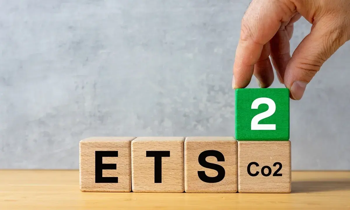 Dłoń układa kostkę z cyfrą 2 na kostce z napisem "CO2", obok kostek z napisami "ETS". Sugeruje to nowy podatek od ogrzewania gazem.
