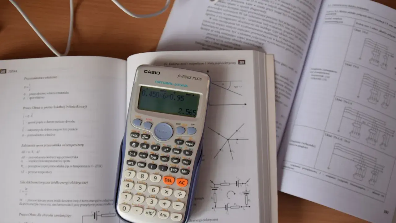 Kalkulator Casio z wyświetlonym wynikiem 2.565, obok otwarta książka z fizyki, gdzie można znaleźć informacje o tym, ile to jest kilowat i jak przeliczyć jednostki.
