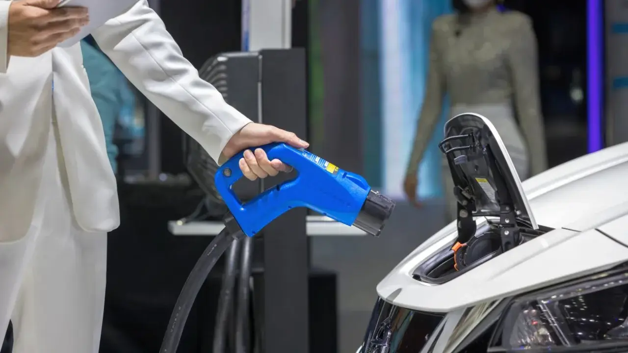 Elektromobilność w zamówieniach publicznych: ładowanie pojazdu elektrycznego. Dłoń trzymająca niebieską wtyczkę ładowarki.