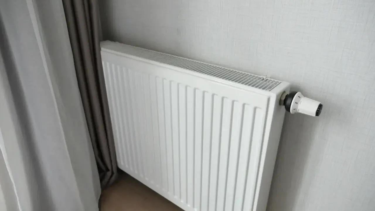 Biały grzejnik panelowy z termostatem, idealny do pokoju 16m2. Obok zasłony.