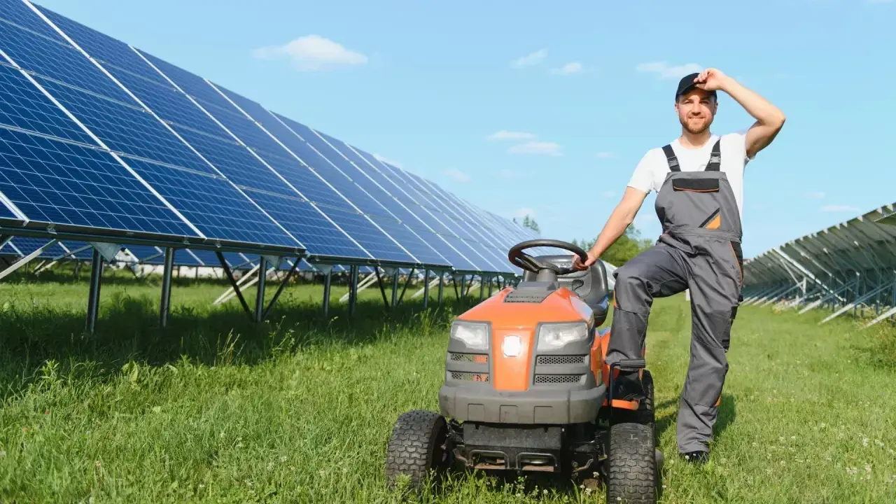 Rolnik w ogrodniczkach odpoczywa przy traktorku, obok rzędy paneli słonecznych zapewniających czystą energię dla wsi.