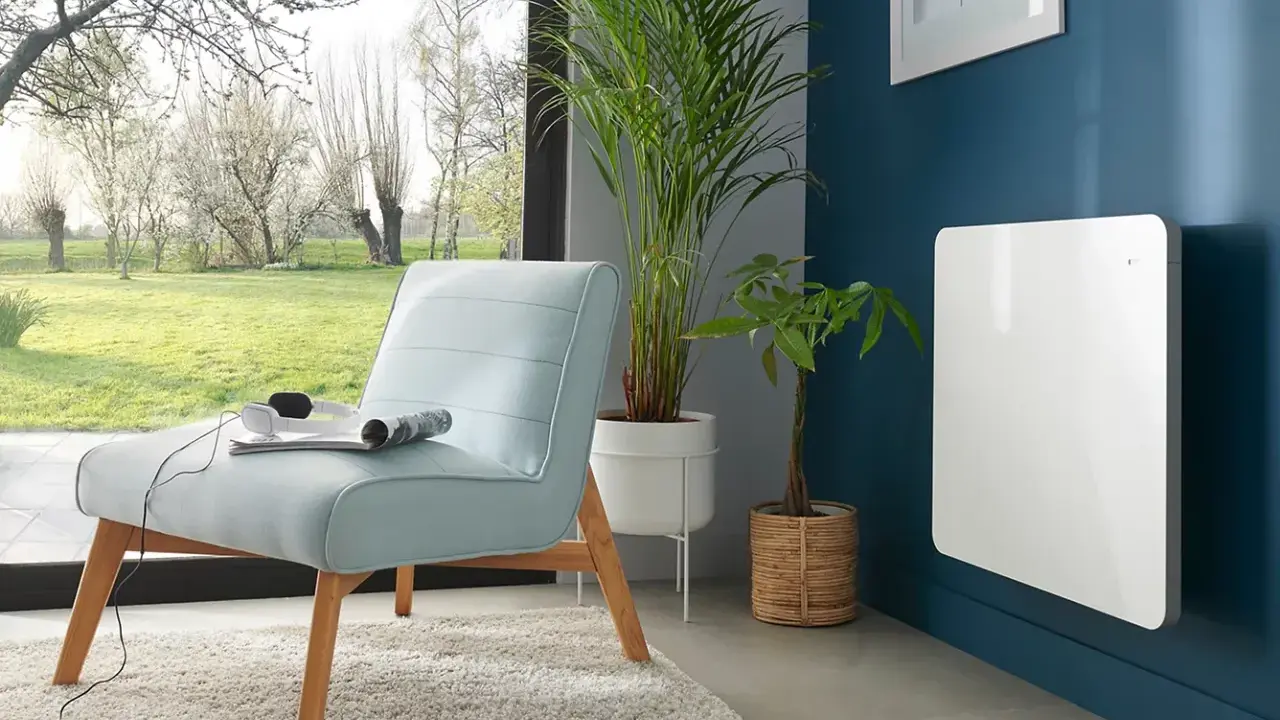 Nowoczesny, biały grzejnik elektryczny na granatowej ścianie. Idealny jako jaki grzejnik do pokoju 10m2, obok jasnoniebieskiej kanapy i roślin.