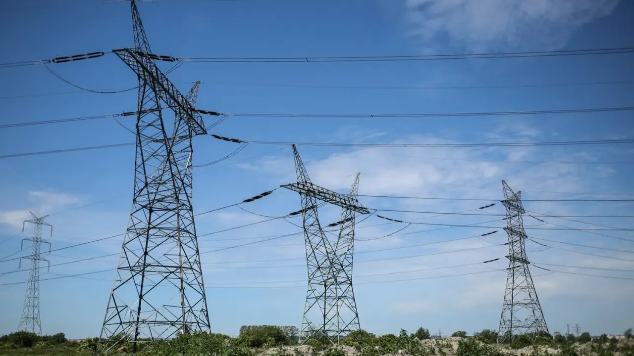 Wysokie wieże energetyczne z przewodami na tle błękitnego nieba z chmurami.
