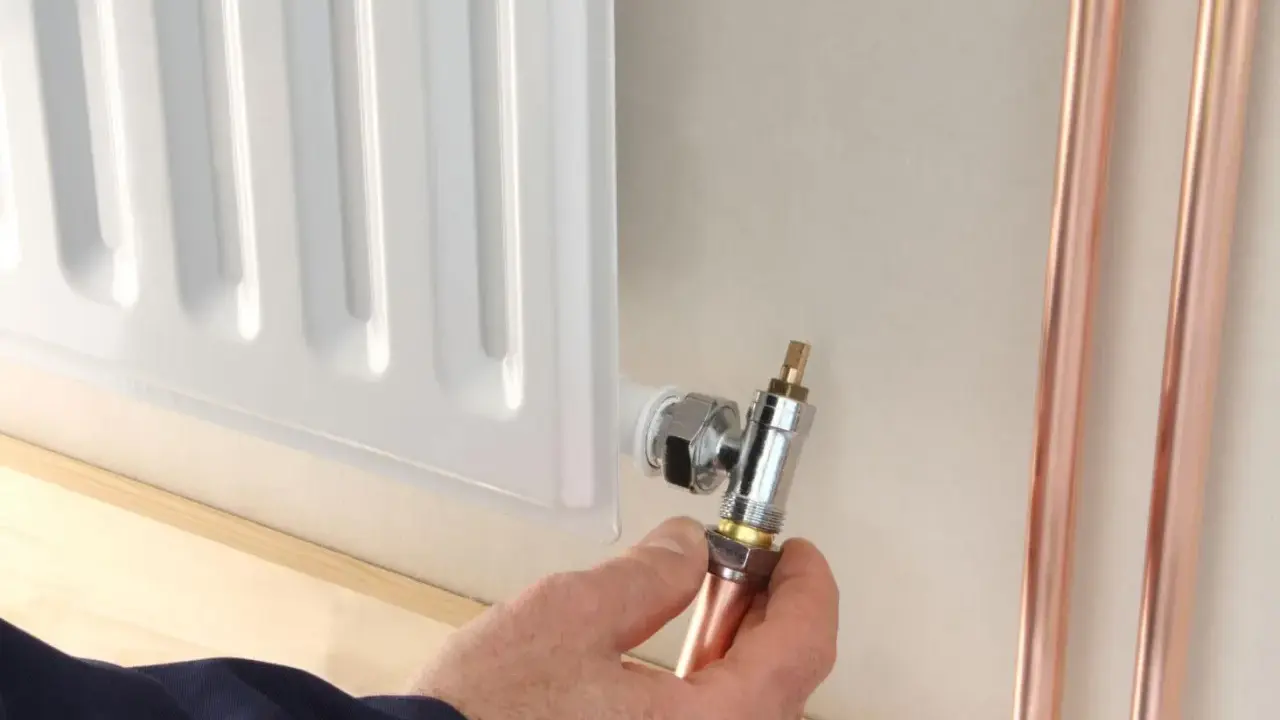 Instalator pokazuje, jak odkręcić dolny zawór grzejnika, trzymając miedzianą rurkę.