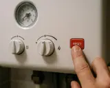 Palec naciska czerwony przycisk RESET na piecu gazowym. Dowiedz się, jak zresetować piec gazowy, gdy wystąpi problem.