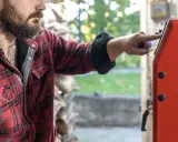Mężczyzna w flanelowej koszuli naciska przycisk na czerwonym piecu. Zastanawia się, jaki piec 20kw na ile metrów będzie najlepszy do jego domu.