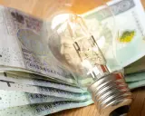 Żarówka leżąca na stosie polskich banknotów 100 zł.