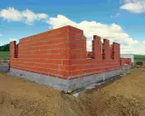 Budowa domu w toku: czerwone ściany z pustaków i betonowy fundament. Czas budowy domu zależy od wielu czynników.