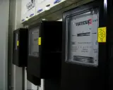 Trzy czarne liczniki energii elektrycznej z cyfrowymi wyświetlaczami i żółtymi naklejkami.