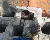 Widok na komin z widocznym metalowym czopuchem i szczotką do czyszczenia. Prawidłowe podłączenie czopucha do komina jest kluczowe dla bezpieczeństwa.