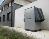 Nowoczesna pompa ciepła Alpha Innotec, kluczowa dla prawidłowego doboru pompy ciepła, stoi przy szarym budynku.