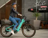 Uśmiechnięta kobieta na turkusowym rowerze elektrycznym. Idealny sposób na skorzystanie z dofinansowania do zakupu roweru elektrycznego i odkrywanie miasta.