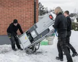 Trzech mężczyzn transportuje nowy piec na wózku. Wymiana pieca w zachodniopomorskim może być konieczna przed zimą.