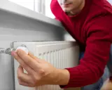 Mężczyzna w czerwonym swetrze reguluje termostat grzejnika. Dobry doradca energetyczny pomoże Ci oszczędzać ciepło.