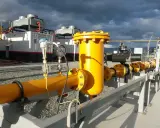 Żółte rury i zawory na tle budynków z chłodnicami, część infrastruktury dla elektrowni gazowych w Polsce.