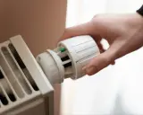 Dłoń reguluje termostat grzejnika. Mimo że termostat ustawiony jest na 0, grzejnik grzeje, co może oznaczać awarię.