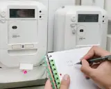 Osoba notuje odczyty liczników energii elektrycznej, przygotowując się do rozliczenia opłaty za przesył prądu.