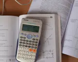 Kalkulator Casio z wyświetlonym wynikiem 2.565, obok otwarta książka z fizyki, gdzie można znaleźć informacje o tym, ile to jest kilowat i jak przeliczyć jednostki.