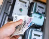 Ręka trzyma polskie banknoty przed licznikami energii. Zastanawiasz się, jak zmienić dostawcę prądu, by oszczędzić?