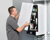 Technik zdejmuje obudowę pieca gazowego dwufunkcyjnego, odsłaniając jego wnętrze.