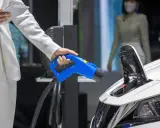Elektromobilność w zamówieniach publicznych: ładowanie pojazdu elektrycznego. Dłoń trzymająca niebieską wtyczkę ładowarki.