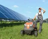 Rolnik w ogrodniczkach odpoczywa przy traktorku, obok rzędy paneli słonecznych zapewniających czystą energię dla wsi.
