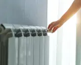 Dłoń reguluje termostat na grzejniku, pokazując różne rodzaje kaloryferów i kontrolę temperatury w domu.
