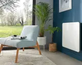 Nowoczesny, biały grzejnik elektryczny na granatowej ścianie. Idealny jako jaki grzejnik do pokoju 10m2, obok jasnoniebieskiej kanapy i roślin.