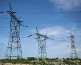 Wysokie wieże energetyczne z przewodami na tle błękitnego nieba z chmurami.