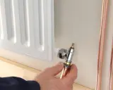 Instalator pokazuje, jak odkręcić dolny zawór grzejnika, trzymając miedzianą rurkę.