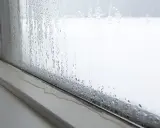 Kondensacja na oknie. Krople wody spływają po szybie, tworząc kałużę na parapecie. To zjawisko, kondensacja, pokazuje różnicę temperatur.