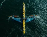 Podwodna turbina wykorzystująca energię pływów, z charakterystycznymi żółto-niebieskimi elementami i pomarańczowymi śmigłami, zanurzona w ciemnych wodach oceanu.