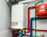 Nowoczesny podłączenie pieca gazowego kondensacyjnego z czerwonym i niebieskim osprzętem, widoczny czerwony zbiornik przeponowy.