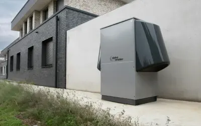 Nowoczesna pompa ciepła Alpha Innotec, kluczowa dla prawidłowego doboru pompy ciepła, stoi przy szarym budynku.