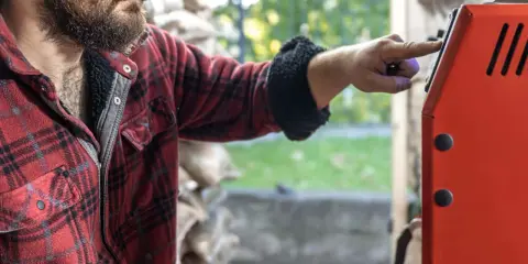 Mężczyzna w flanelowej koszuli naciska przycisk na czerwonym piecu. Zastanawia się, jaki piec 20kw na ile metrów będzie najlepszy do jego domu.