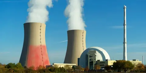 Dwie chłodnie kominowe i kopuła elektrowni konwencjonalnej na tle błękitnego nieba.