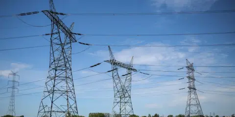 Wysokie wieże energetyczne z przewodami na tle błękitnego nieba z chmurami.