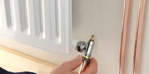 Instalator pokazuje, jak odkręcić dolny zawór grzejnika, trzymając miedzianą rurkę.
