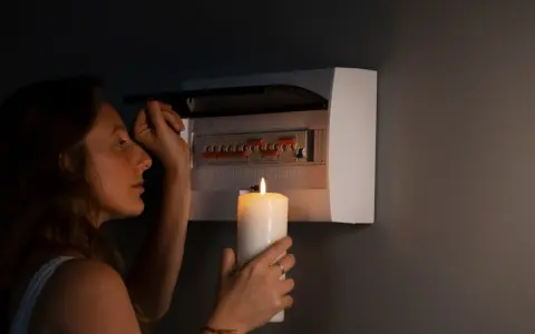 Kobieta z zapaloną świecą przy skrzynce z bezpiecznikami. Czy to black out?