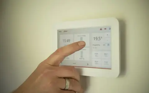 Dłoń dotyka ekranu termostatu, pokazując temperaturę 19,5°C. Ustawienia ogrzewania pomogą określić, jak często powinien włączyć się piec gazowy.