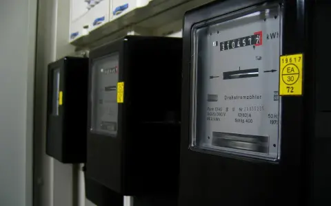 Trzy czarne liczniki energii elektrycznej z cyfrowymi wyświetlaczami i żółtymi naklejkami.