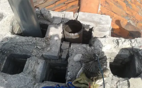 Widok na komin z widocznym metalowym czopuchem i szczotką do czyszczenia. Prawidłowe podłączenie czopucha do komina jest kluczowe dla bezpieczeństwa.