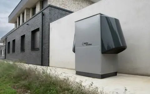 Nowoczesna pompa ciepła Alpha Innotec, kluczowa dla prawidłowego doboru pompy ciepła, stoi przy szarym budynku.
