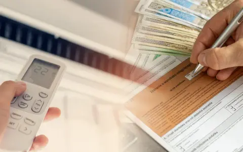 Ręka trzymająca pilot do klimatyzacji, obok stos banknotów i formularz podatkowy. Czy klimatyzację można odliczyć od podatku?
