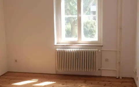 Jasne, oto opis:

Drewniana podłoga, biały grzejnik i parapet nad nim. Za oknem widać drzewa.