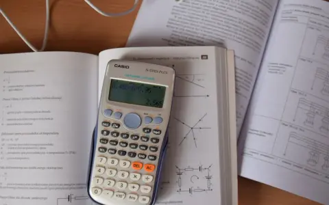 Kalkulator Casio z wyświetlonym wynikiem 2.565, obok otwarta książka z fizyki, gdzie można znaleźć informacje o tym, ile to jest kilowat i jak przeliczyć jednostki.